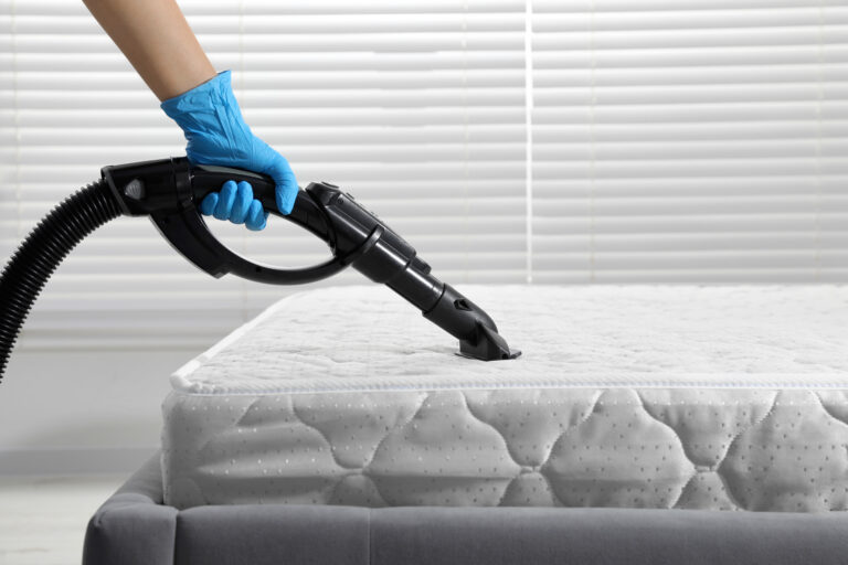 Woman disinfecting mattress with vacuum cleaner indoors, closeup